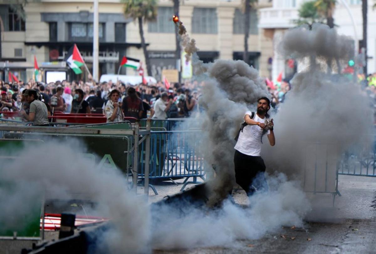 A man throws a smoke flare back at police after Pro-Palestinians protestors invaded the street  forcing race organisers to abandon the 21st and final stage of the Vuelta a Espana 2025, in Madrid on September 14, 2025.    Thomas COEX / AFP