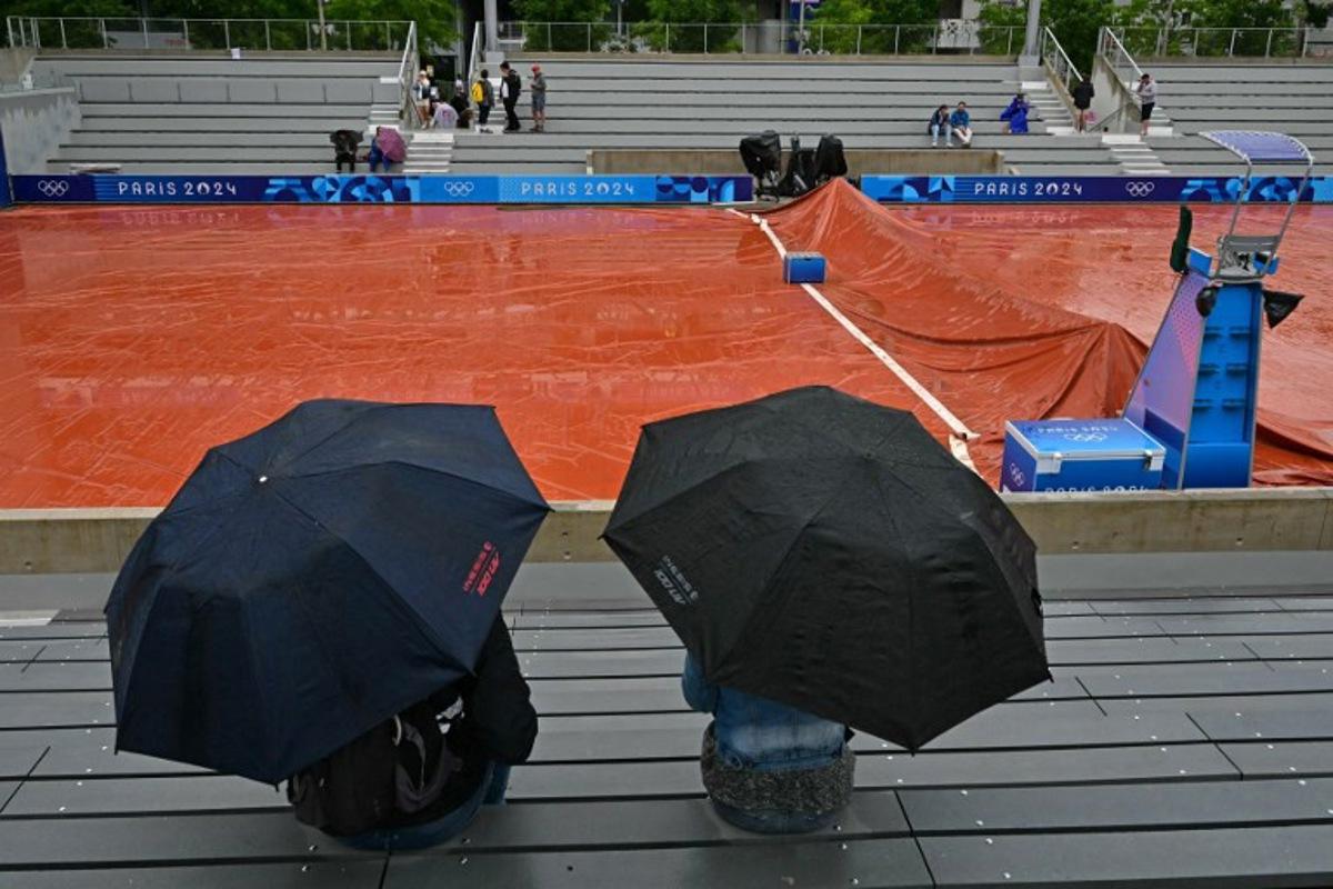 Spectators take shelter from the rain as the wet weather delays the start of play on the outside courts at the Roland-Garros Stadium at the Paris 2024 Olympic Games, in Paris on July 27, 2024.   Miguel MEDINA / AFP