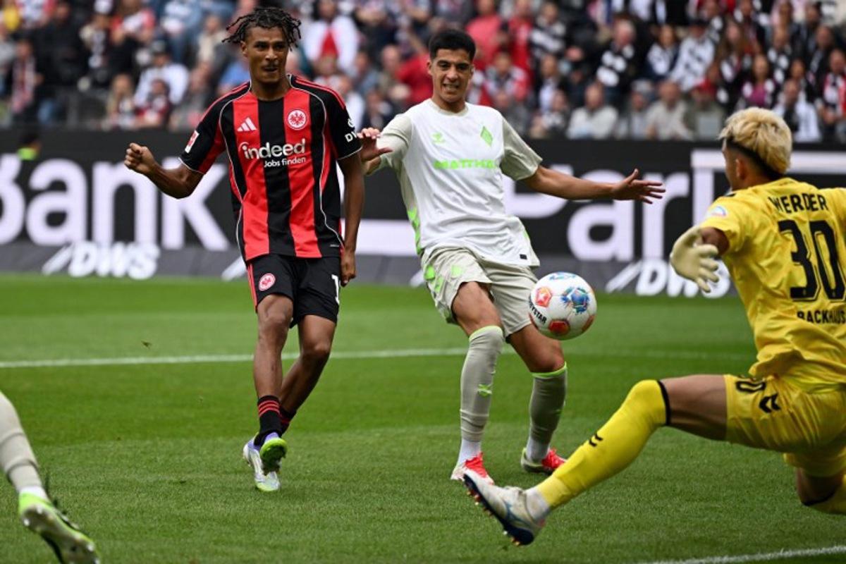 Frankfurt's French forward #19 Jean-Matteo Bahoya (L) scores his team's third goal past Bremen's German goalkeeper #30 Mio Backhaus (R) during the German first division Bundesliga football match between Eintracht Frankfurt and Werder Bremen in Frankfurt am Main, western Germany on August 23, 2025.  Kirill KUDRYAVTSEV / AFP