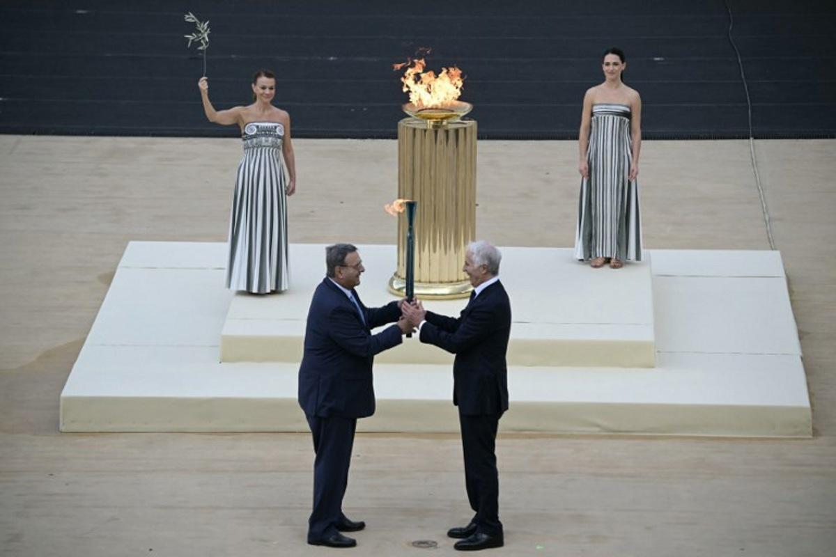 Hellenic Olympic Committee President Isidoros Kouvelos (L) and President of the Italian National Olympic Committee and CEO of the Milan Cortina 2026 Winter Olympic Giovanni Malago (R) hand the torch next to Greek actress Mary  Mina playing the role of the High Priestess, during the handover Olympic flame ceremony for the Milano-Cortina 2026 Winter Olympic Games and Paralympic Games, at the Panathinean stadium in Athens, on December 4, 2025.  Angelos Tzortzinis / AFP