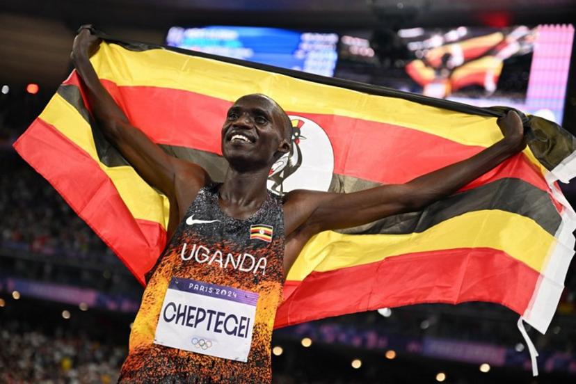 Winner Uganda's Joshua Cheptegei celebrates with the Uganda's national falg after crossing the finish line in the men's 10000m final of the athletics event at the Paris 2024 Olympic Games at Stade de France in Saint-Denis, north of Paris, on August 2, 2024. Uganda's Joshua Cheptegei sets a new Olympic record in the men's 10000m. Kirill KUDRYAVTSEV / AFP