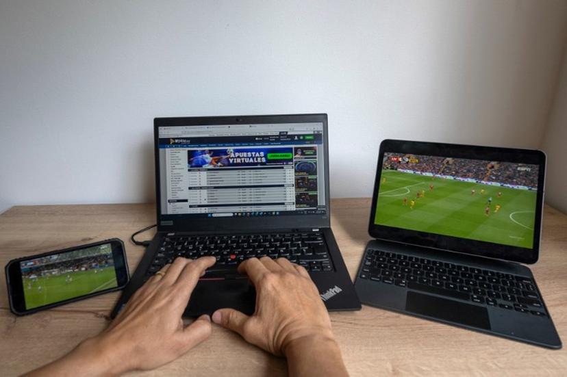 In this photo illustration taken on February 20, 2025, a user checks the betting company Wplay on a laptop while watching a football match in Bogota on February 17, 2025.  For the first time, online sports betting will pay sales tax in Colombia. The worst armed conflict crisis in decades prompted the government to tax this important sector of the economy in a decision that strikes a chord with football fans. Luis ACOSTA / AFP