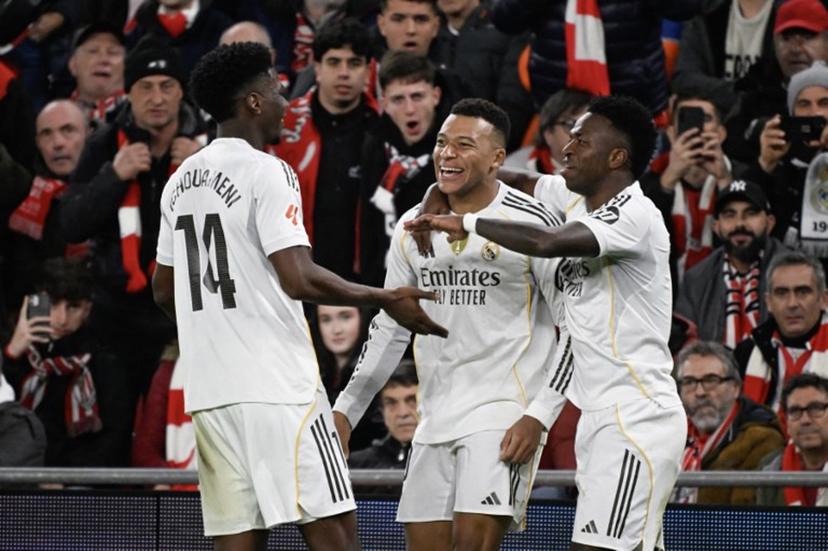 Real Madrid's French forward #10 Kylian Mbappe (C) celebrates with teammates Real Madrid's Brazilian forward #07 Vinicius Junior (R) and Real Madrid's French midfielder #14 Aurelien Tchouameni after scoring his team's third goal during the Spanish league football match between Athletic Club Bilbao and Real Madrid CF at the San Mames stadium in Bilbao on December 3, 2025.  ANDER GILLENEA / AFP