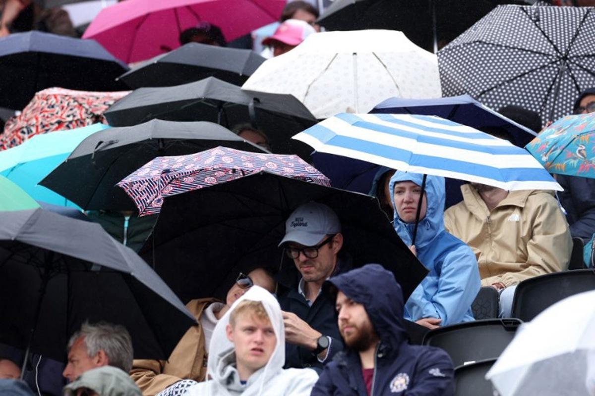 People shelter under umbrella's as a rain delay suspends the round of 32, singles match at the HSBC WTA tennis Championships at Queen's Club in west London on June 8, 2026.  Adrian Dennis / AFP