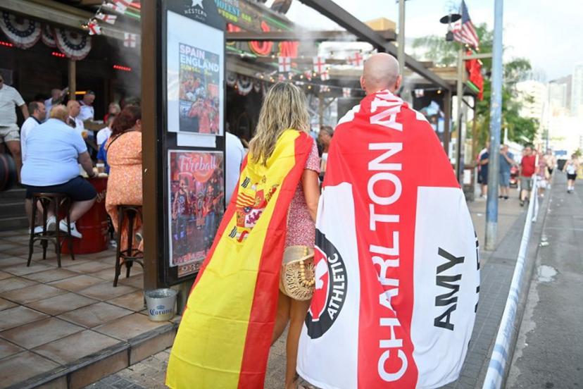 Fans wrapped in England's Charlton Athletic Football Club and Spain's flags walk prior the UEFA Euro 2024 finale football match between Spain and England, in Benidorm, eastern coast of Spain, on July 14, 2024.  JOSE JORDAN / AFP