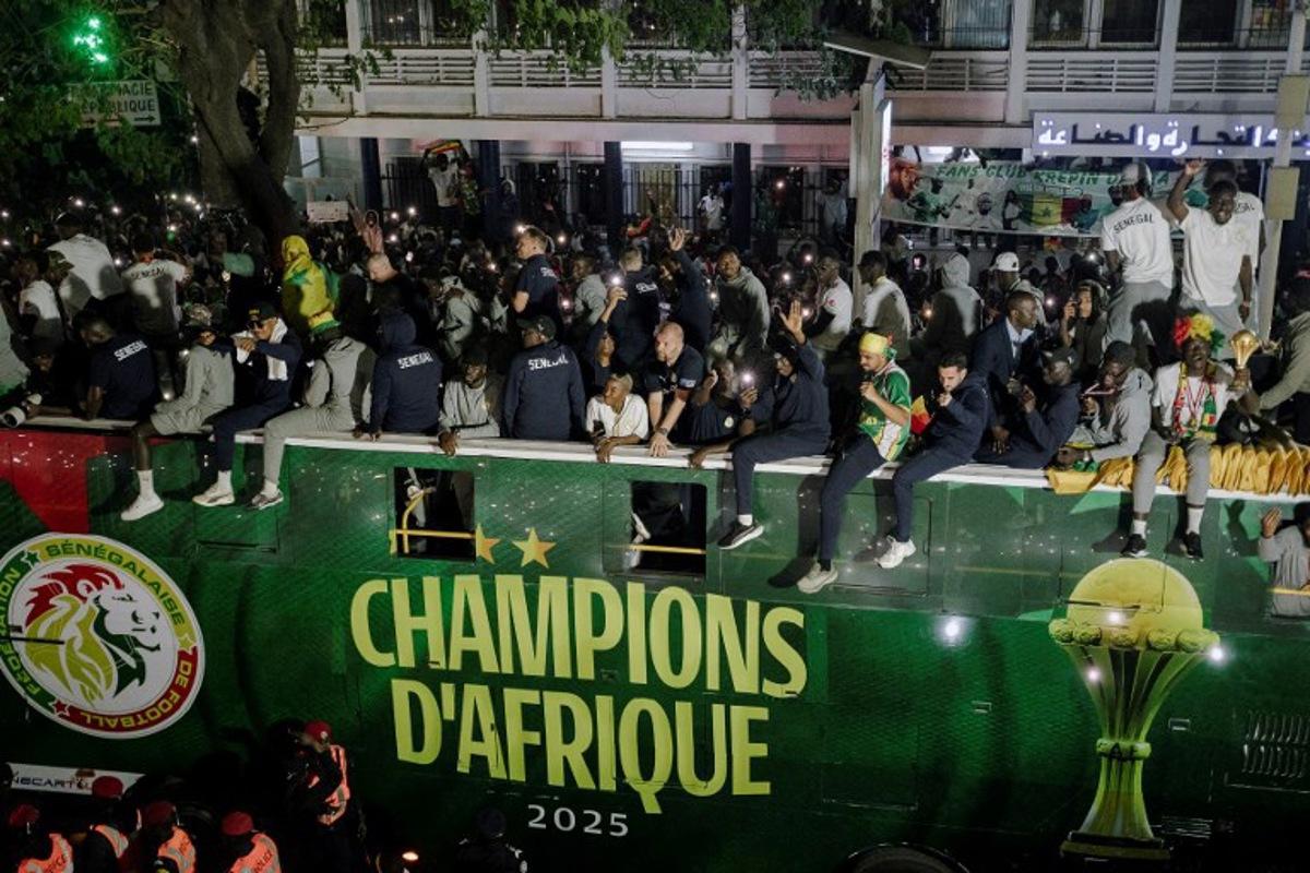 Senegal's Football Team players celebrate winning the Africa Cup of Nations (CAN) atop an open bus during a trophy parade in the streets of Dakar on January 20, 2026. Senegal's national football team, crowned African Nations champion thanks to its victory over Morocco on January 18 in Rabat after a high-octane final, landed late on January 19 night back home, where it was warmly welcomed off the plane by the Senegalese head of state and his government. Carmen Abd Ali / AFP