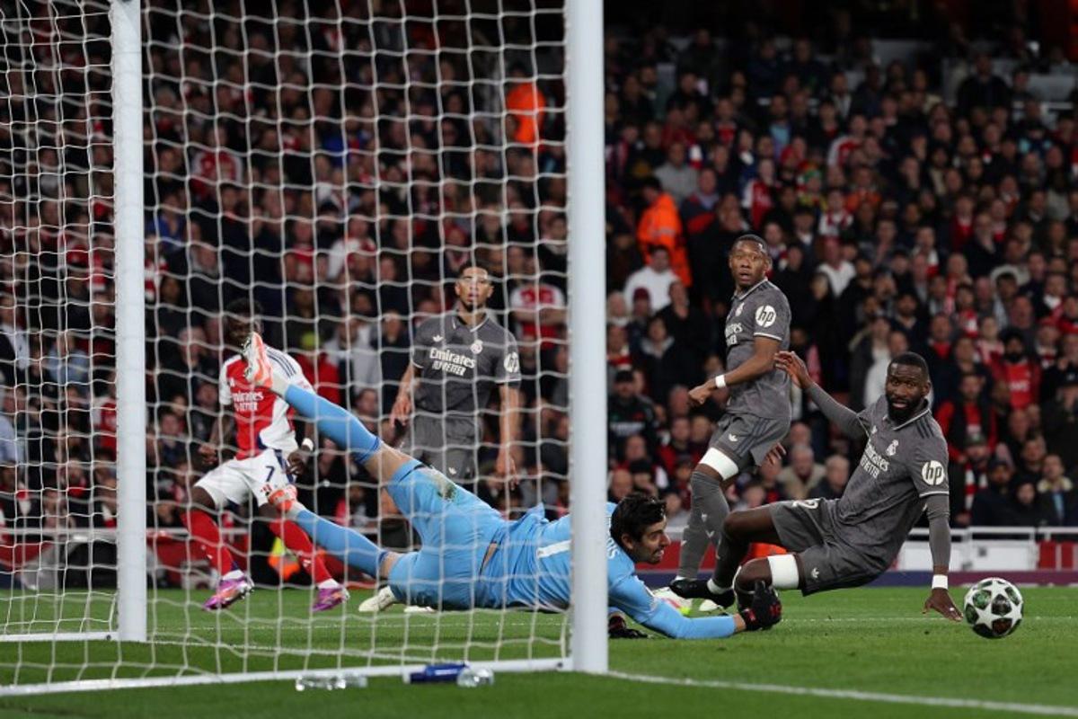Real Madrid's Belgian goalkeeper #01 Thibaut Courtois saves a shot from Arsenal's English midfielder #07 Bukayo Saka during the UEFA Champions League Quarter final first leg football match between Arsenal and Real Madrid, at the Emirates Stadium, in London, on April 8, 2025.   Adrian Dennis / AFP