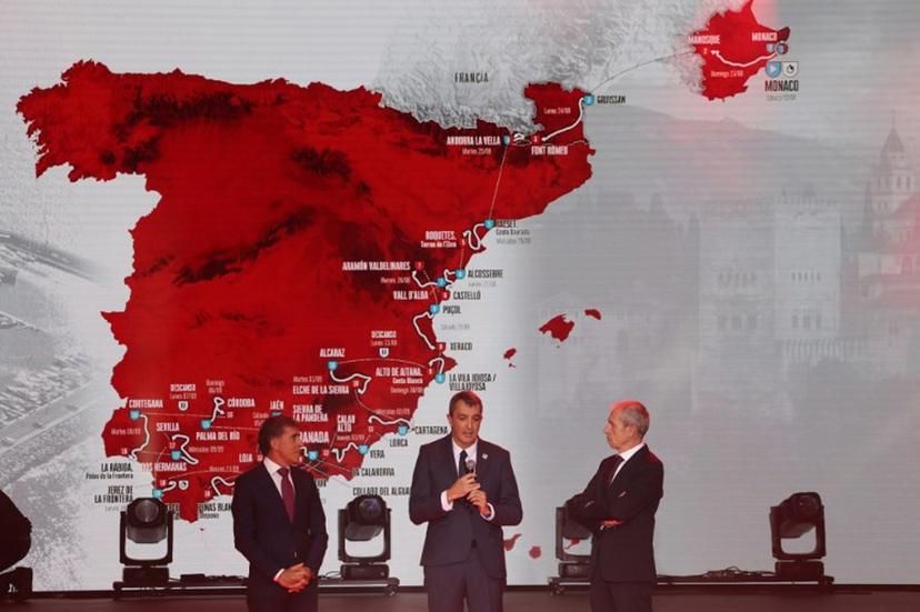 Race director of La Vuelta, Javier Guillen (C) speaks, flanked by Sports journalist Carlos de Andres (R) and Spanish former cyclist Pedro Delgado as the race itinerary is displayed on a screen during the presentation of the 81th edition of 'La Vuelta' cycling tour of Spain, in Monaco on December 17, 2025. The 2026 Vuelta a Espana will start with a time-trial in Monaco and finish in Granada, after organisers on December 17, 2025 unveiled what they say will be one of the most difficult routes in the race's history. Valery HACHE / AFP