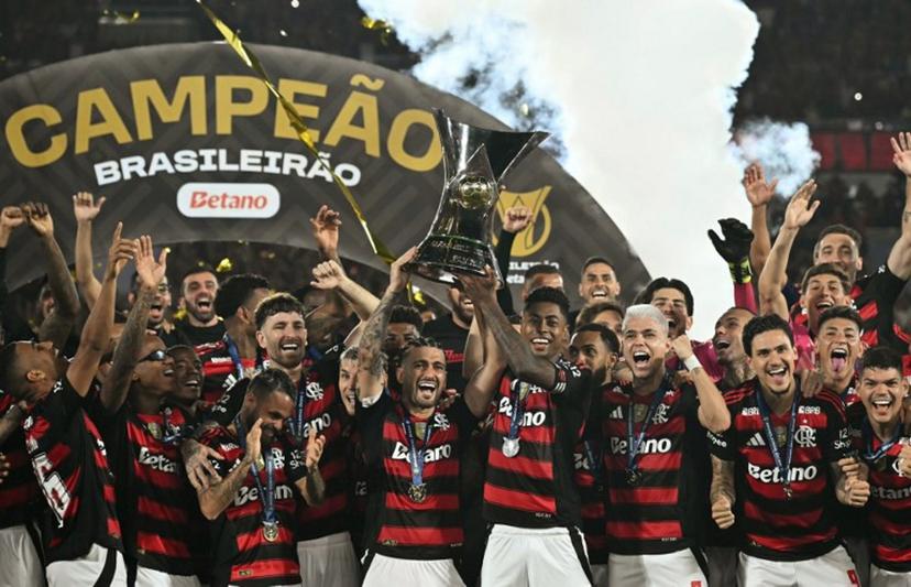Flamengo's Uruguayan midfielder #10 Giorgian de Arrascaeta (C-L) and forward #27 Bruno Henrique (C-R) lift the Brasileirao trophy after winning the Brasileirao Serie A football match between Flamengo and Ceara at Maracana Stadium in Rio de Janeiro, Brazil, on December 3, 2025.  Mauro PIMENTEL / AFP