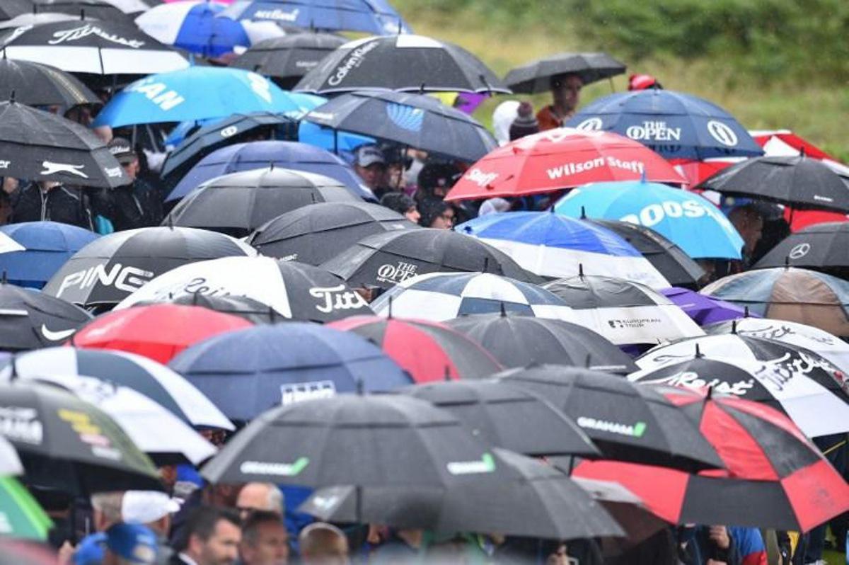 Spectators shelter under umbrellas during the second round of the British Open golf Championships at Royal Portrush golf club in Northern Ireland on July 19, 2019.  Glyn KIRK / AFP RESTRICTED TO EDITORIAL USE

