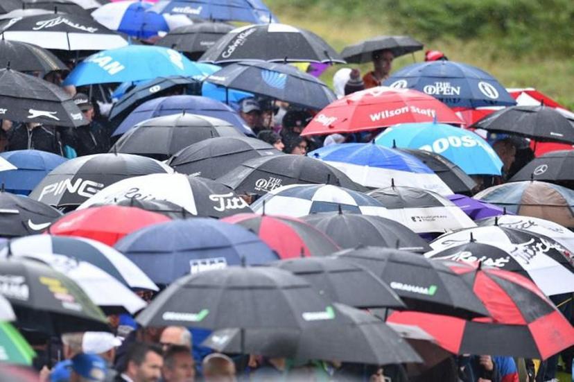 Spectators shelter under umbrellas during the second round of the British Open golf Championships at Royal Portrush golf club in Northern Ireland on July 19, 2019.  Glyn KIRK / AFP RESTRICTED TO EDITORIAL USE


