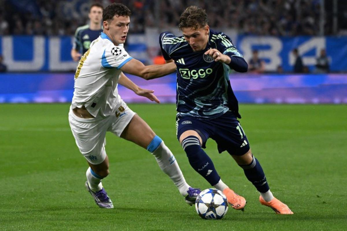 Marseille's French defender #28 Benjamin Pavard (L) and Ajax's Belgian forward #11 Mika Godts fight for the ball during the UEFA Champions League, league phase day 2, football match between Olympique de Marseille (FRA) and AFC Ajax (NED) at the Velodrome stadium, in Marseille on September 30, 2025.  Miguel MEDINA / AFP