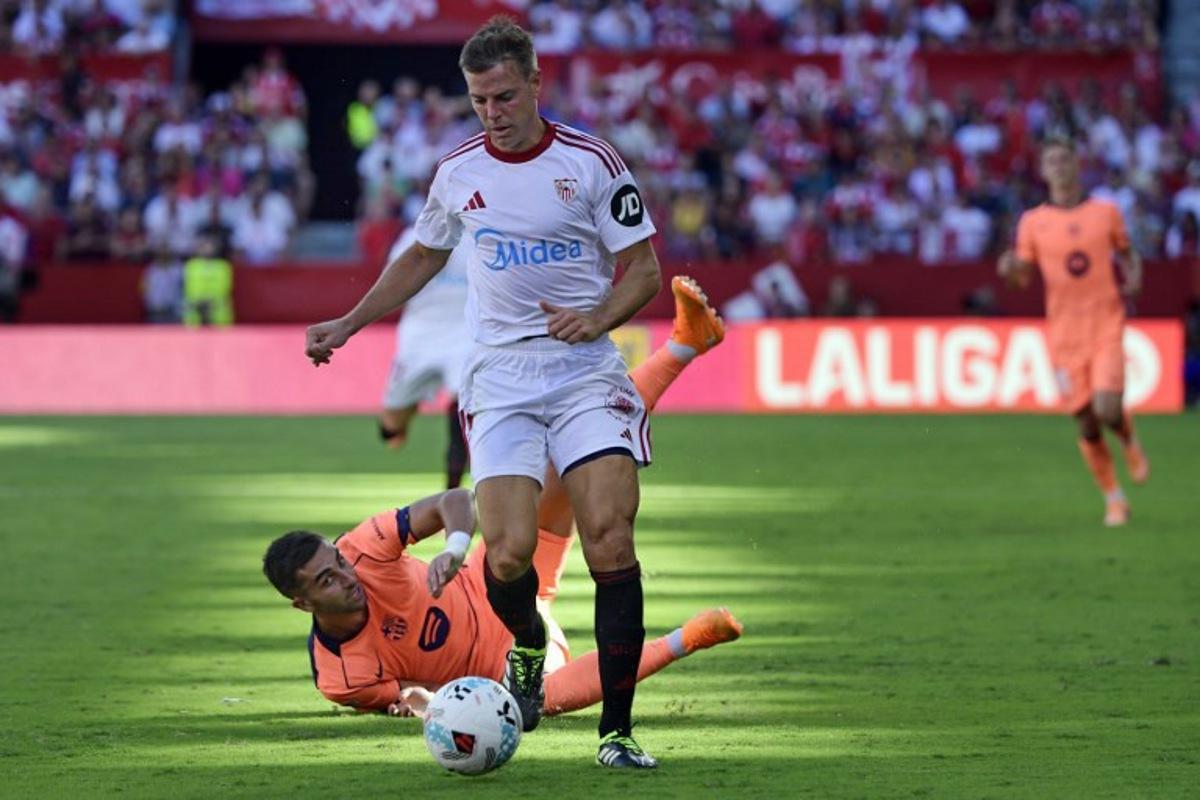 Sevilla's Spanish defender #03 Cesar Azpilicueta and Barcelona's Spanish forward #07 Ferran Torres (BOTTOM) fight for the ball during the Spanish league football match between Sevilla FC and FC Barcelona at Ramon Sanchez Pizjuan Stadium in Seville on October 5, 2025. CRISTINA QUICLER / AFP